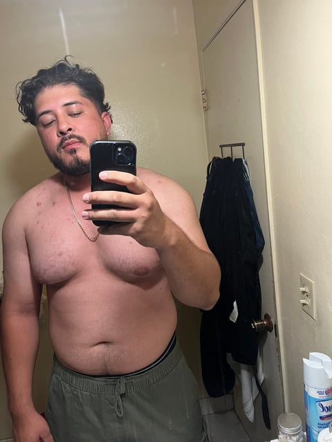 Shirtless man taking a mirror selfie in a bathroom, holding a smartphone